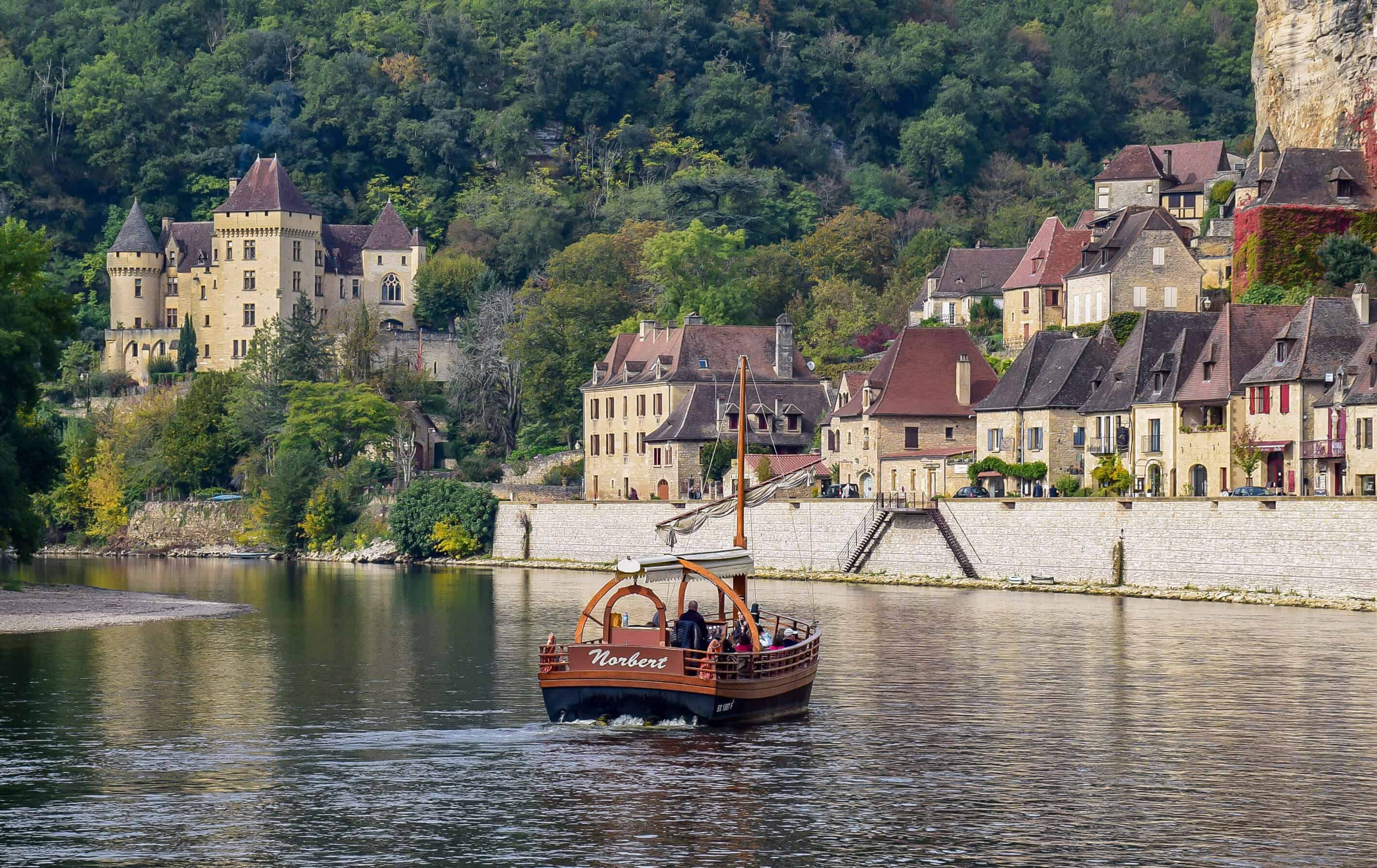 Boat sailing toward the medieval village and castle of Rocque Gageac in the Dordogne region of France