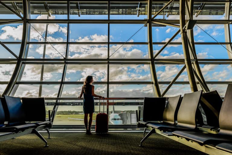 A woman with a bag in an airport observing steps to stay healthy while traveling.