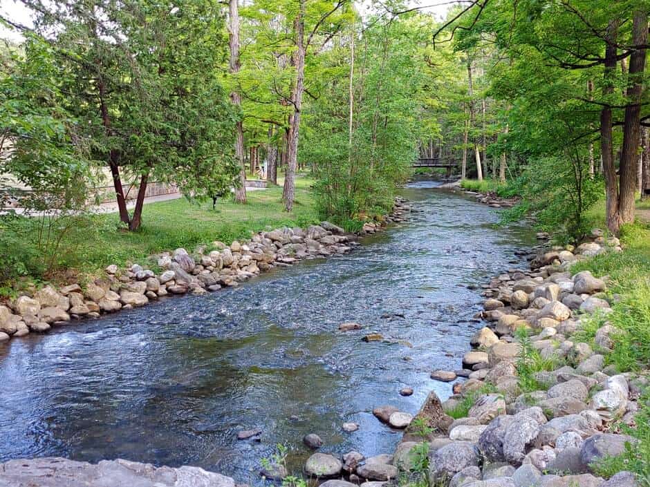 A creek lined by trees and boulders, with a bridge in Saratoga Springs NY
