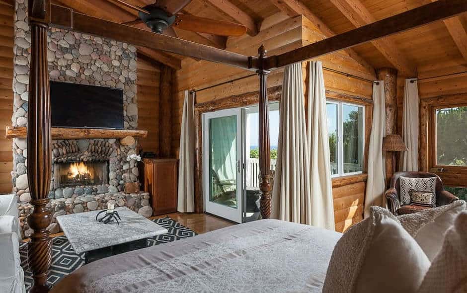 Four-poster bed in front of fireplace in rustic cabin