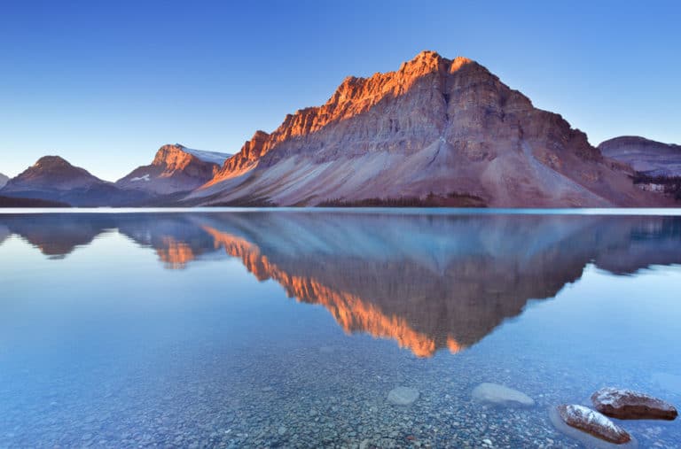 Sunlight on the top of a large triangular mountain reflecting on water in Banff National Park